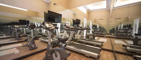 Un gimnasio con varias cintas de correr, bicicletas estáticas y elípticas.