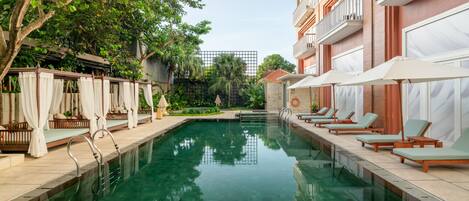 A pool area with lounge chairs and a pergola with white curtains.
