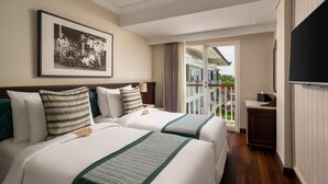 Habitación de hotel con dos camas, un balcón, un televisor y una foto en un marco en la pared.