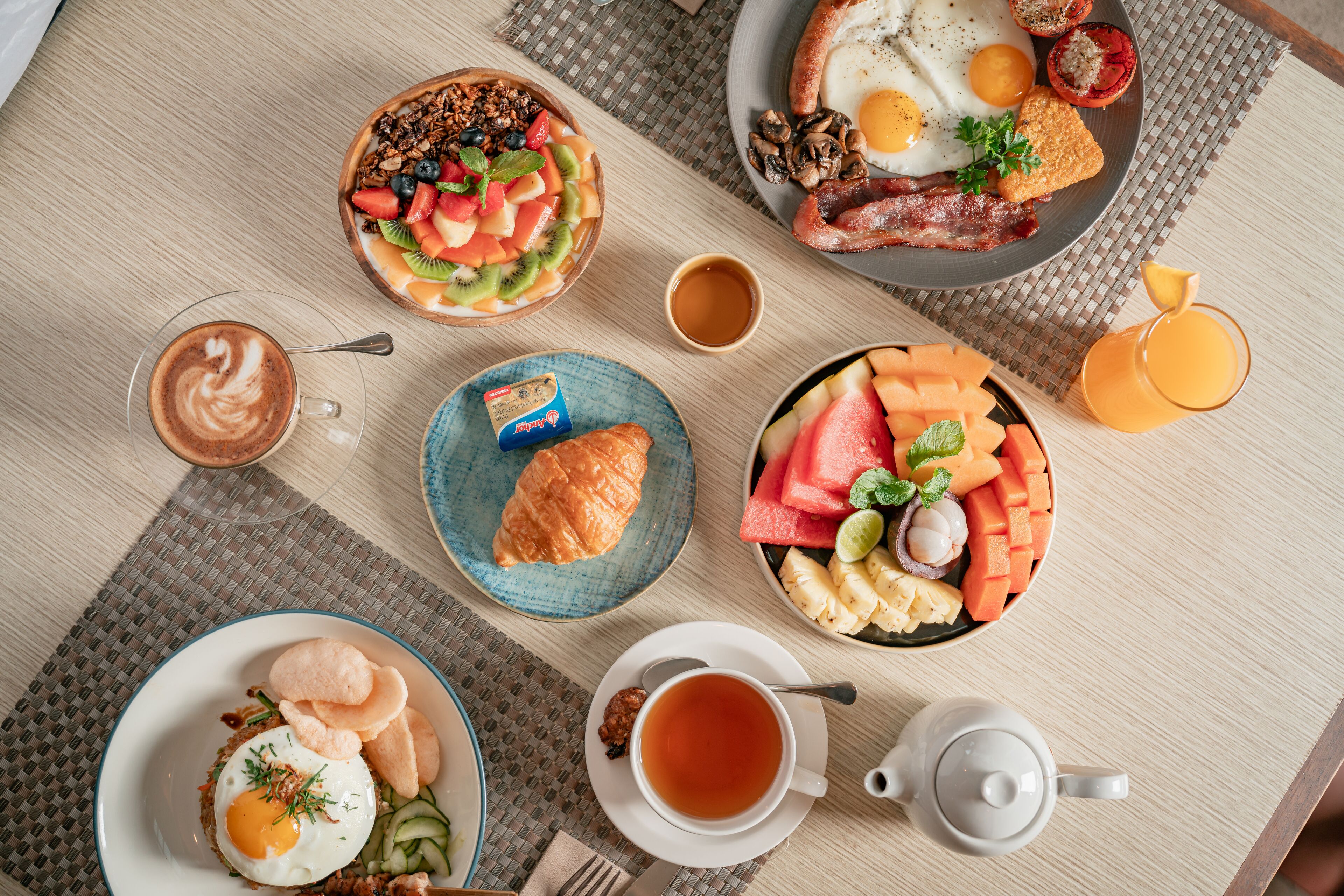 Ein reichhaltiges Frühstücksbuffet auf einer Holztischplatte mit verschiedenen Speisen, darunter Eier, Toast und Obst.