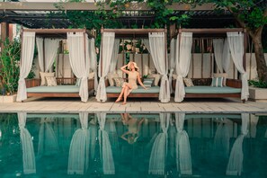 Un área de piscina tranquila al aire libre con una cama con dosel y agua cristalina.