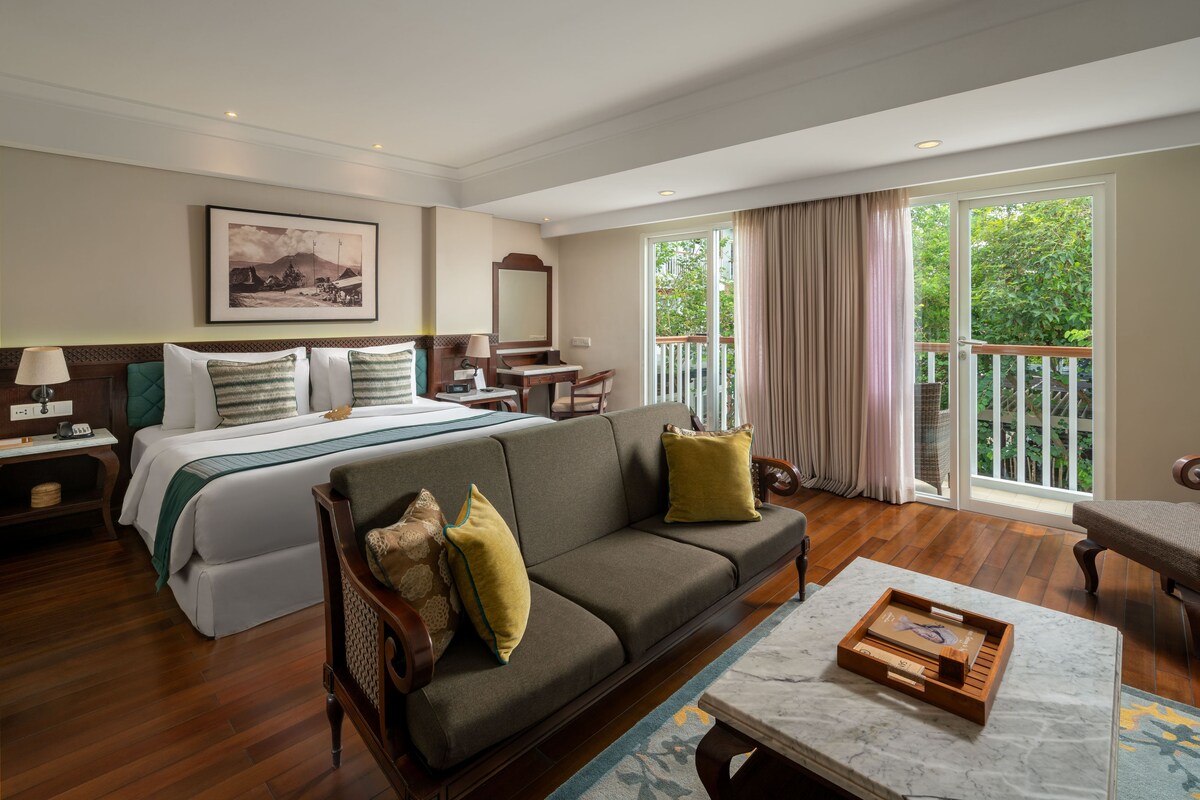 A hotel room with a bed, a sofa, a desk, and a balcony with curtains.