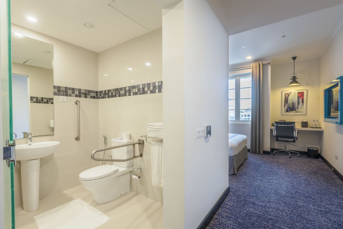Un baño moderno con ducha, inodoro y lavabo, un pequeño escritorio con silla y una ventana con cortinas.