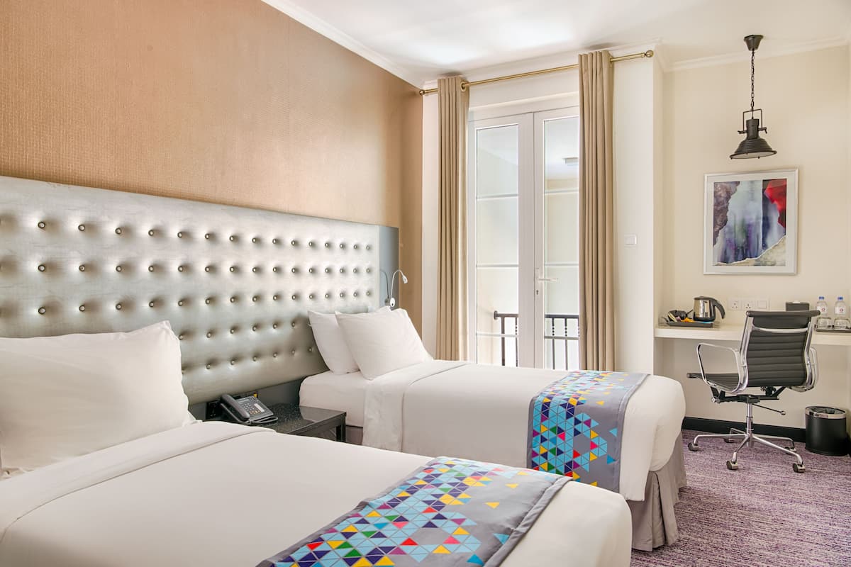 Habitación de hotel con dos camas, cabecero, escritorio con silla, teléfono y un cuadro en la pared.