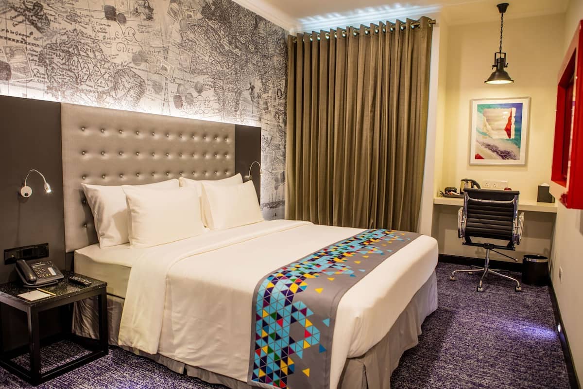 Habitación de hotel con una cama grande, un escritorio, una silla, un mapa en la pared y un cuadro.