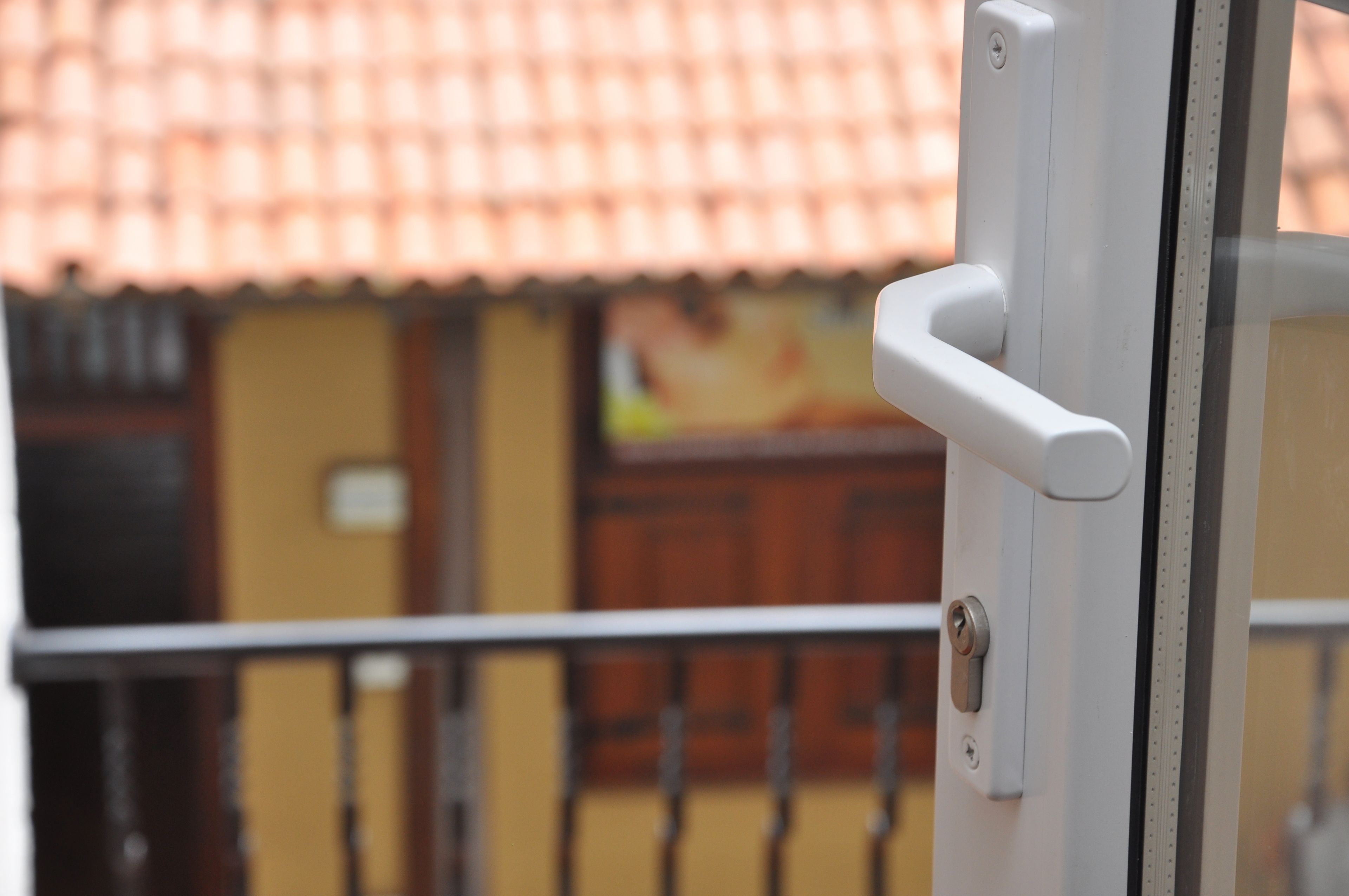 Una puerta con manija y cerradura, una barandilla metálica y un edificio con techo de tejas al fondo.