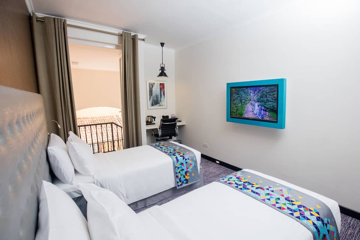 Habitación de hotel con dos camas, un escritorio, una silla, un televisor y una ventana con cortinas.