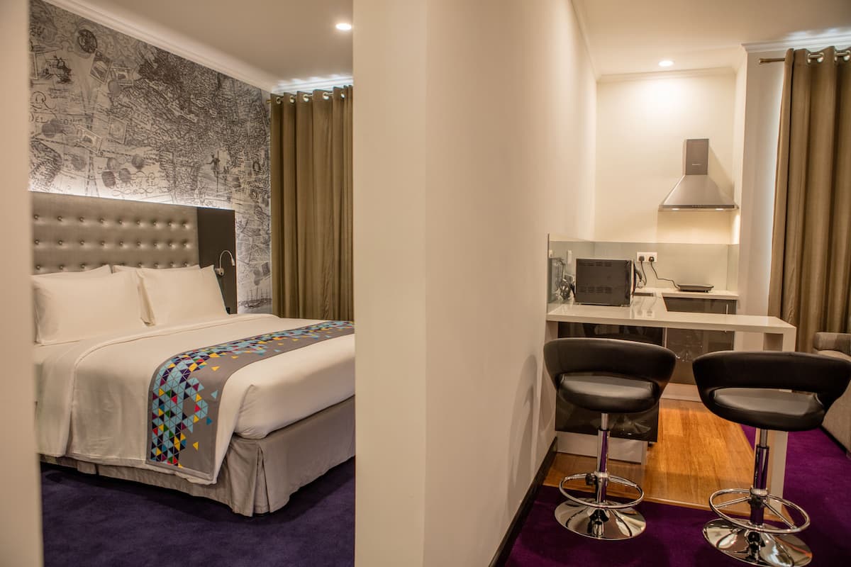 Habitación de hotel con cama, escritorio, dos sillas y zona de ducha.