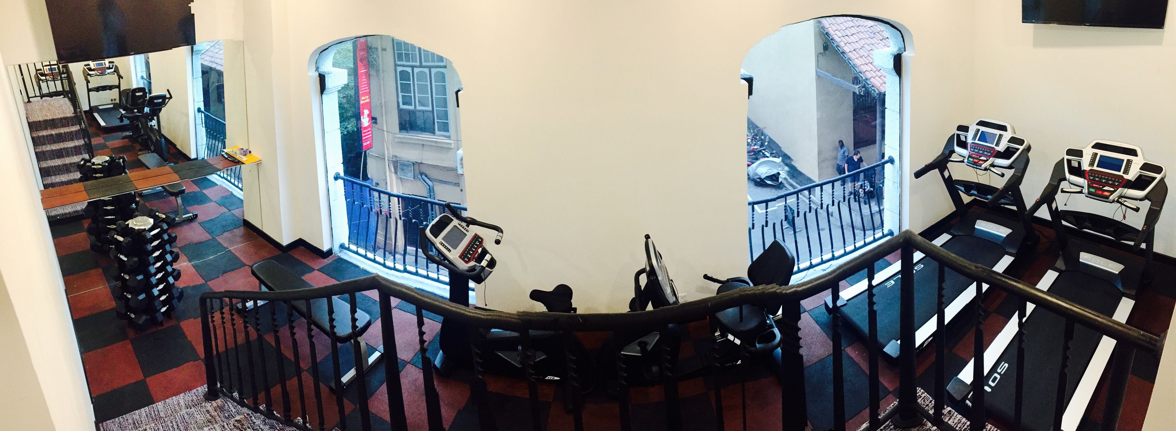 A gym with treadmills and weights, a staircase with a checkered floor, and a view of the street outside.