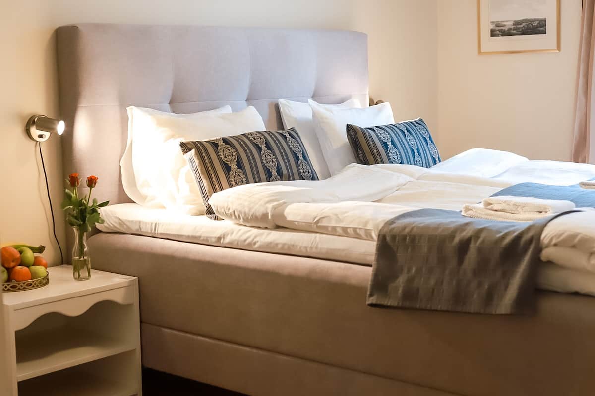 A neatly made bed with white and patterned pillows, a bedside table with a vase of flowers, and a lamp.