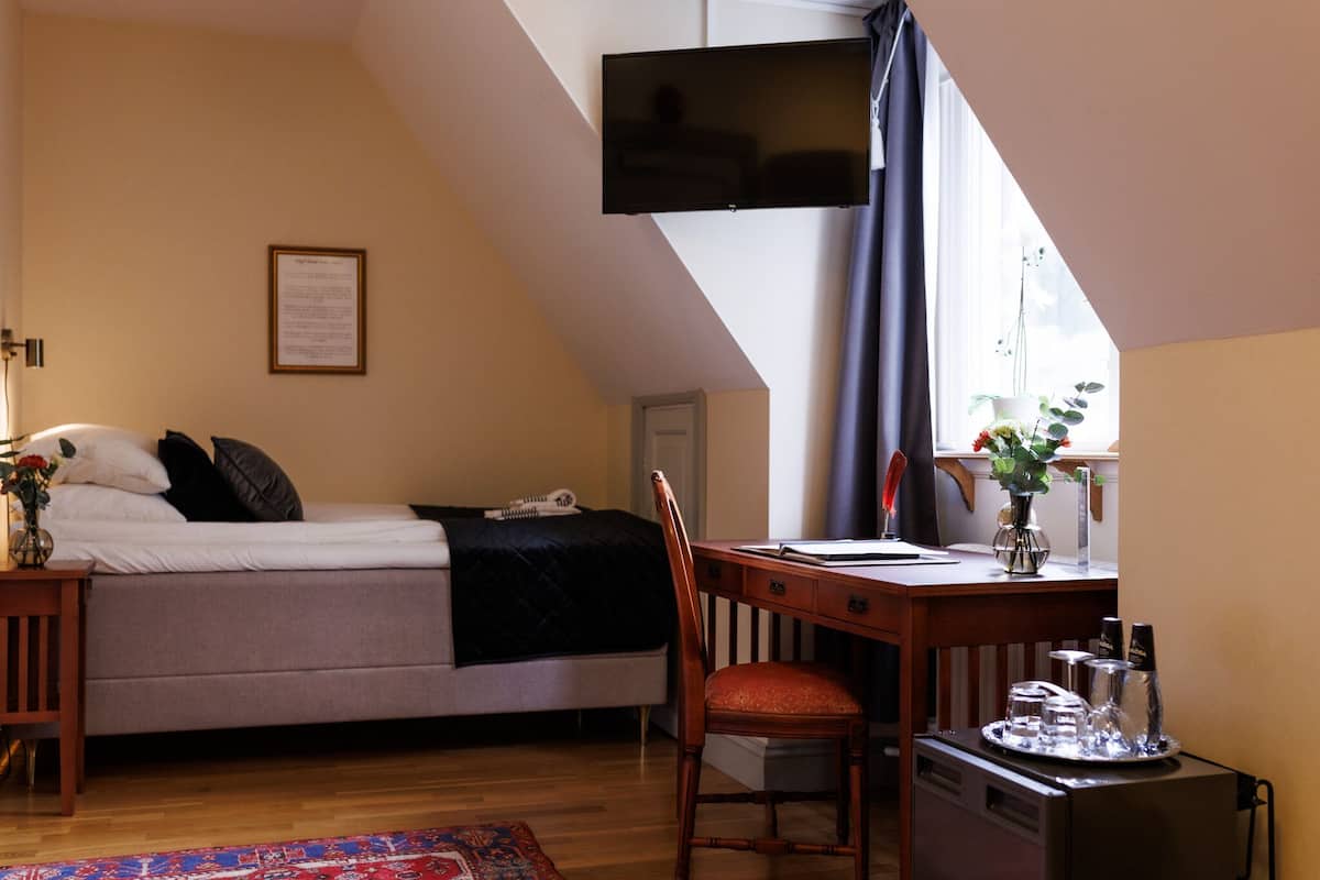 A bedroom with a bed, desk, chair, and a TV mounted on the wall.