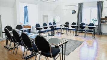 A conference room with multiple tables and chairs, a clock on the wall, and a window with curtains.