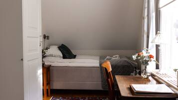 Un dormitorio pequeño y acogedor con una cama individual, una silla de madera, una mesita y una ventana con vistas.