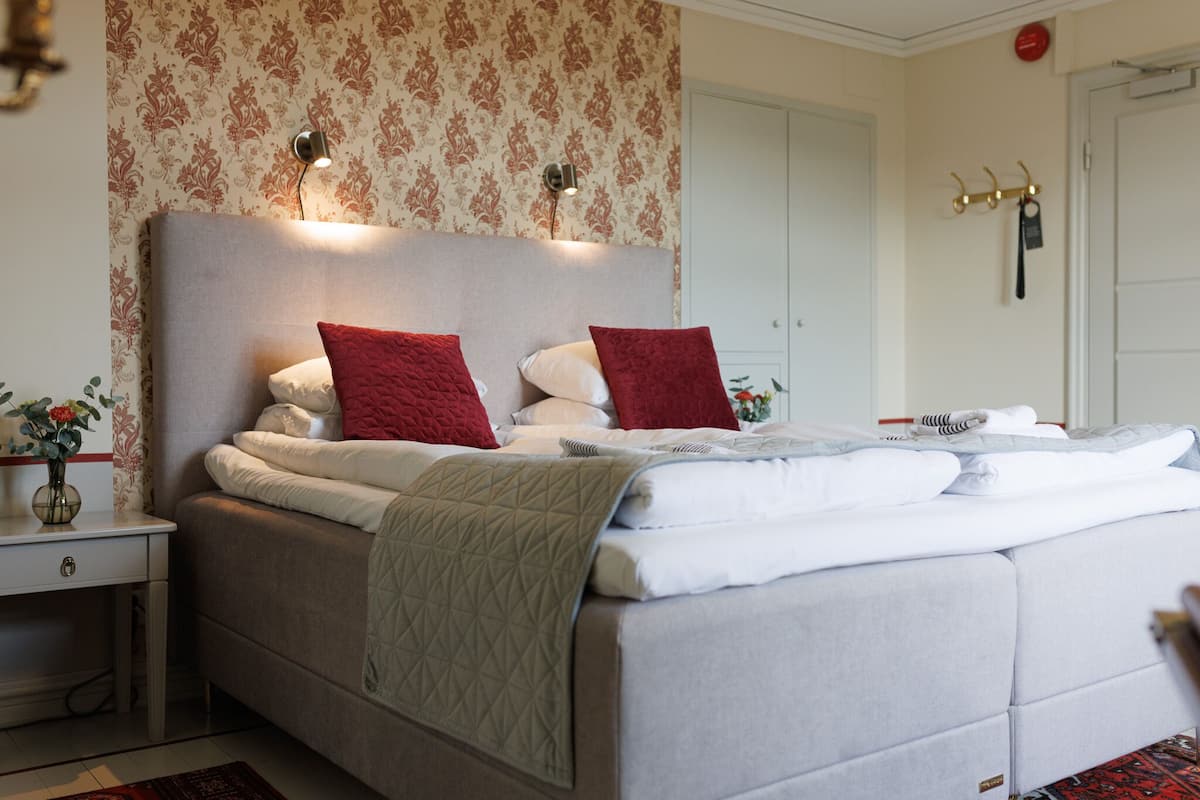A neatly made bed with a quilted blanket, two red pillows, and a headboard with wall-mounted lights.
