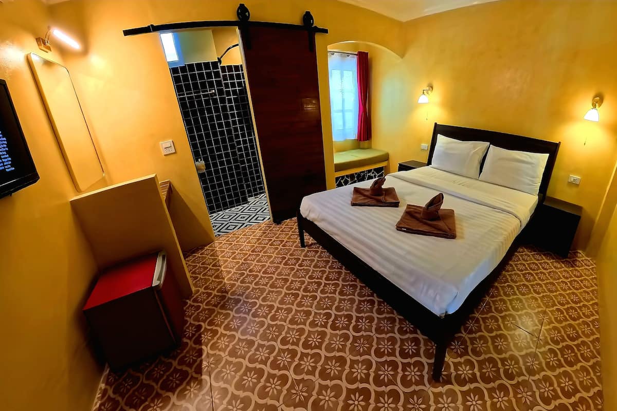 Habitación de hotel con cama, una pequeña zona de estar, un espejo y televisor montado en la pared.