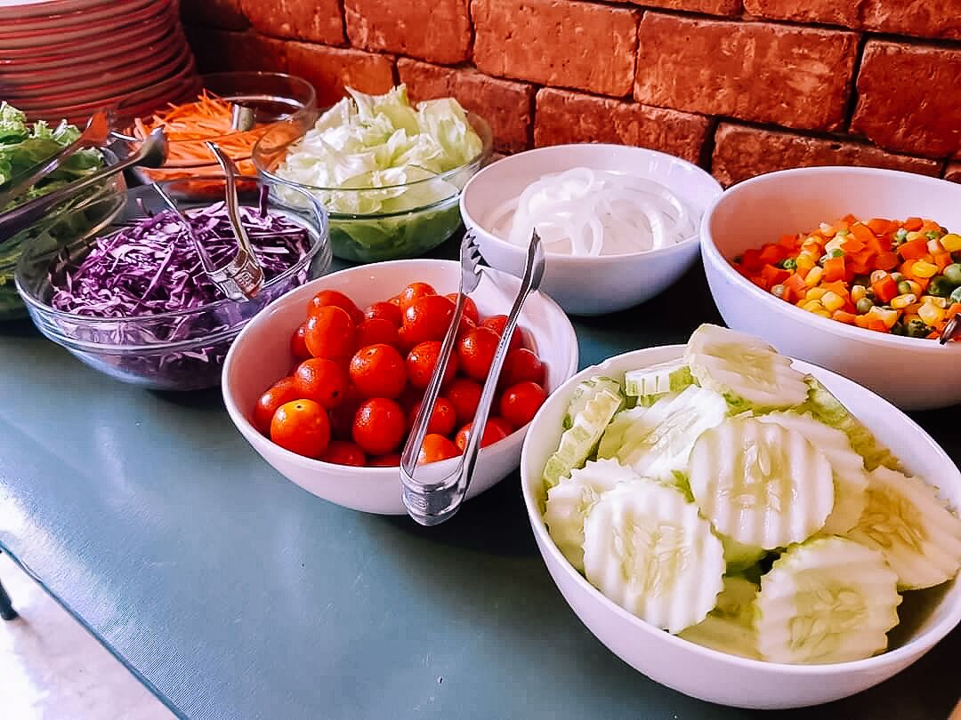 Una mesa con varios recipientes de ingredientes para ensalada, como tomates, repollo y zanahorias.