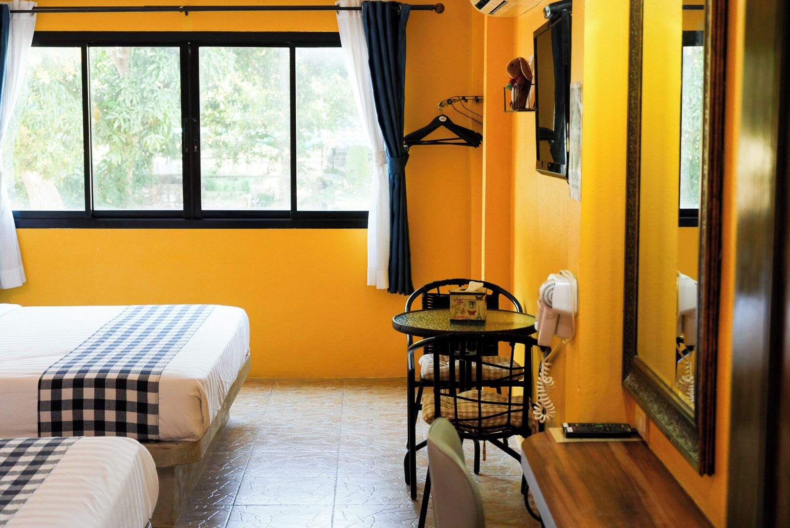 Ein Hotelzimmer mit zwei Betten, einem kleinen Tisch mit einem Stuhl, einem Föhn und einem Fenster mit Vorhängen.
