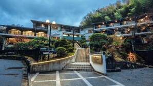 Ein Hotel Eingang mit einer Treppe, die zu einem Gebäude führt, umgeben von Grünflächen und einem bewölkten Himmel.