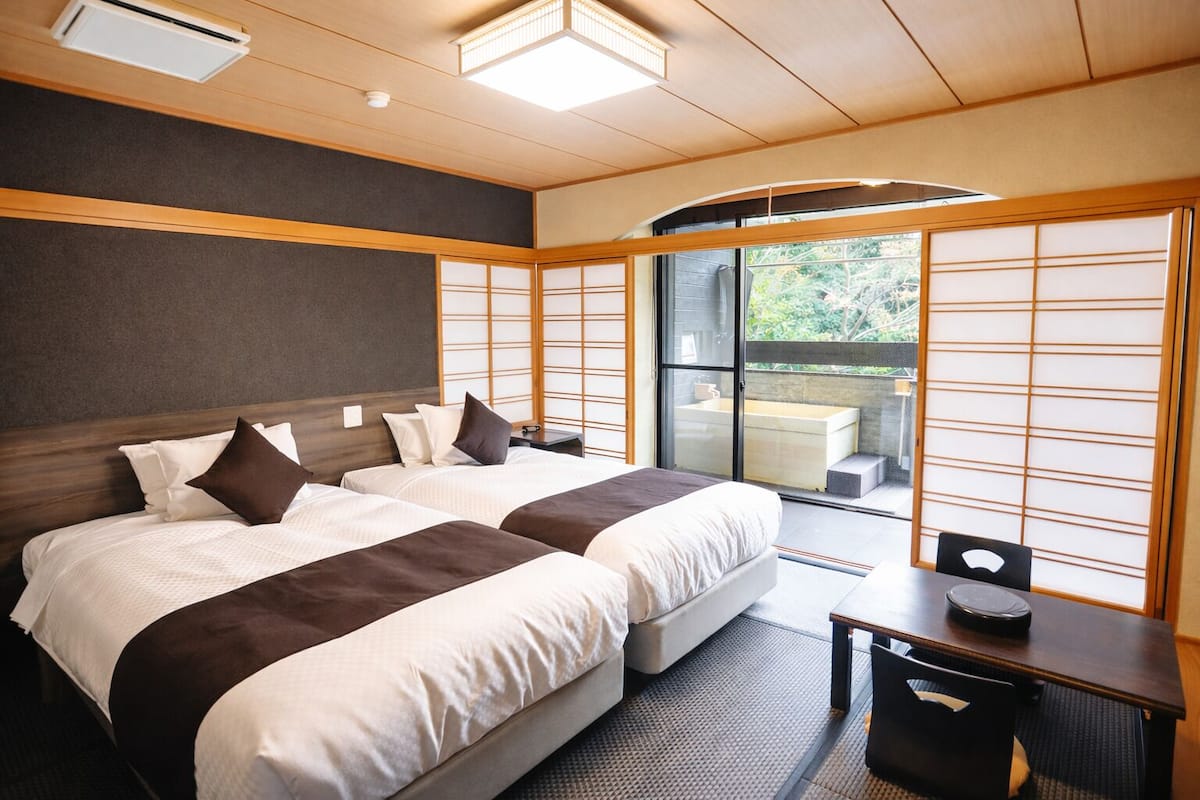 Ein Hotelzimmer mit zwei Betten, einem Schreibtisch, einem Stuhl und einer Glastür, die auf einen Balkon führt.