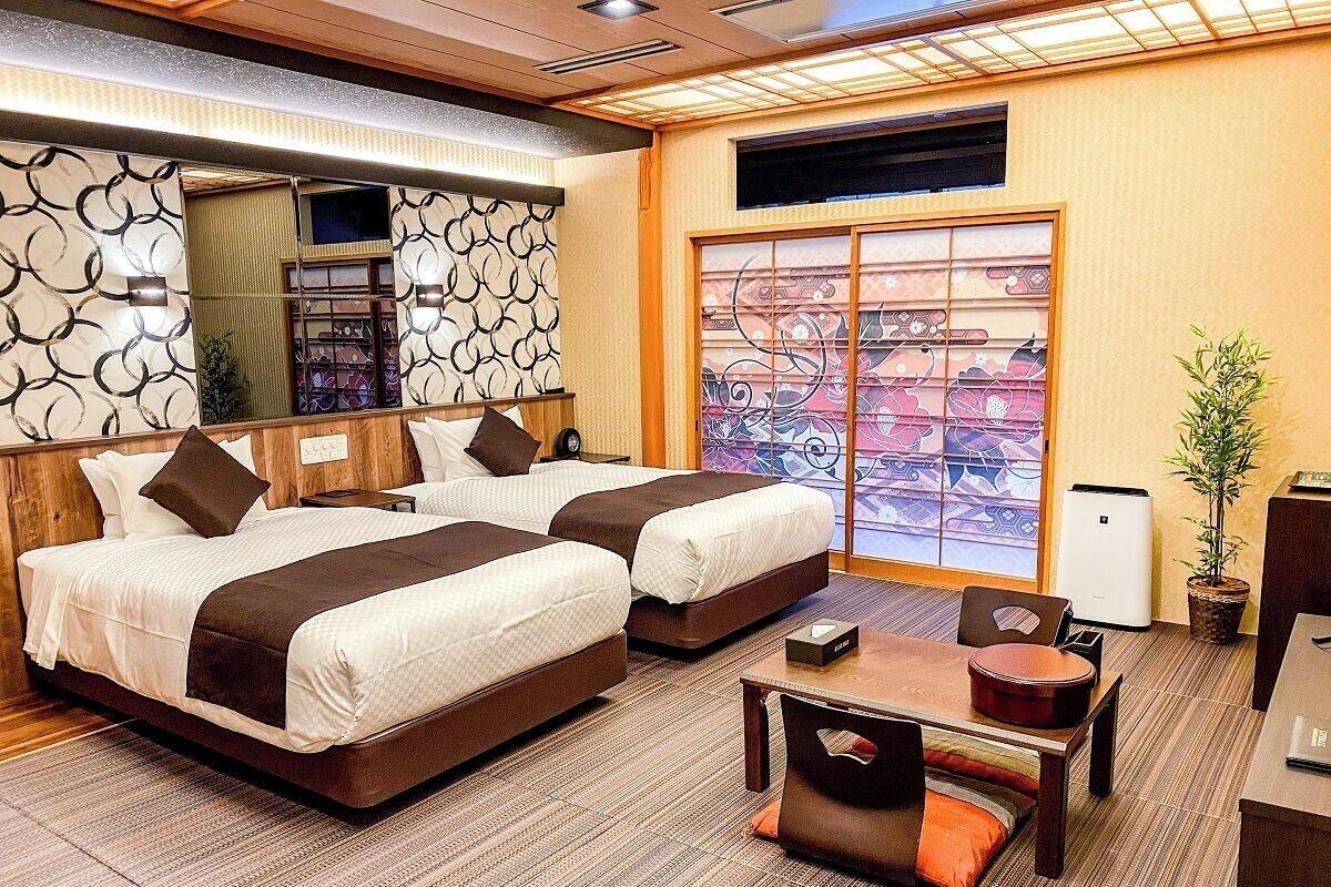 Ein Hotelzimmer mit zwei Betten, einem kleinen Tisch, einem Sessel, einer Topfpflanze und einer Glastür mit Blick.