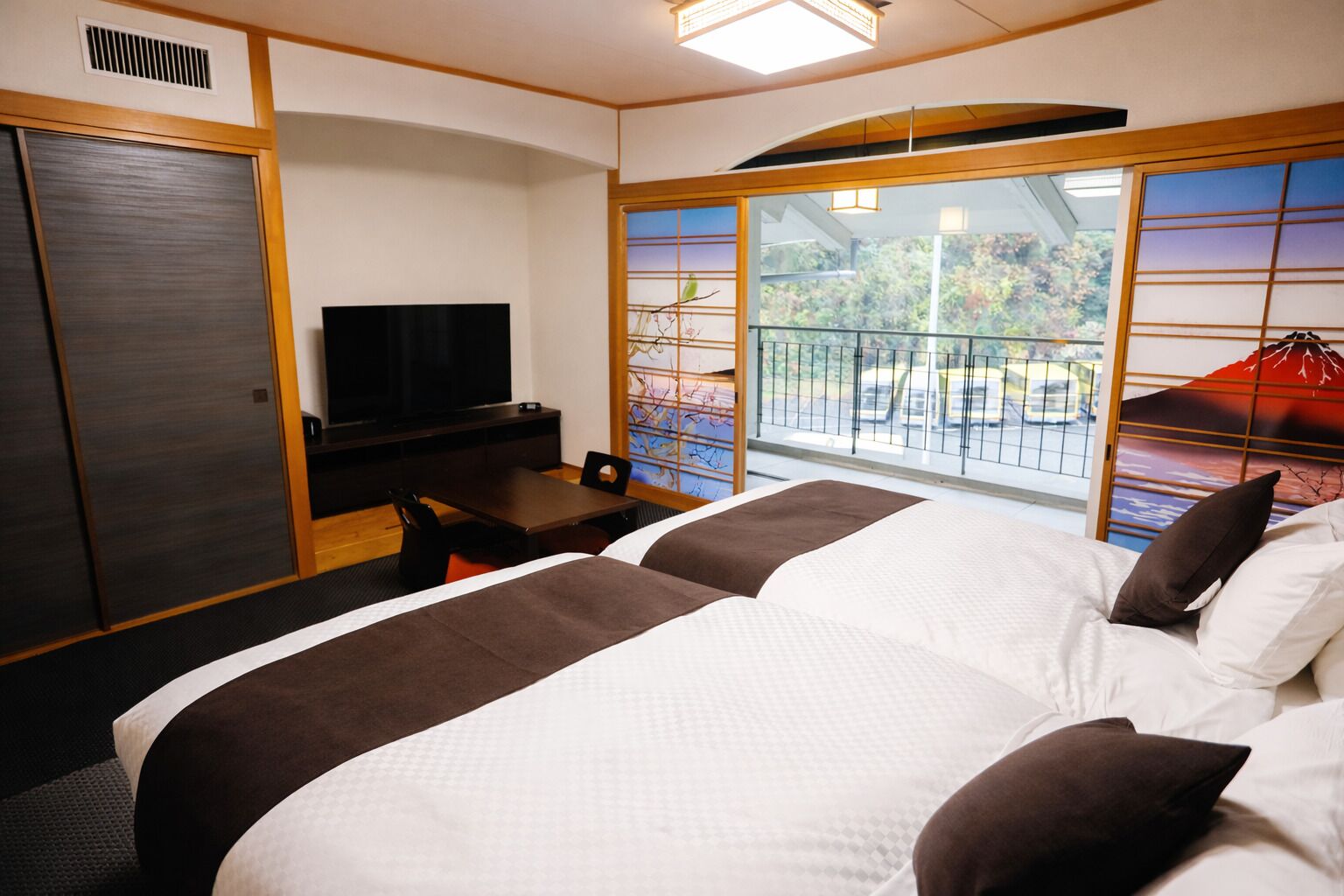 A hotel room with two beds, a TV, a desk, and a view of the outdoors.