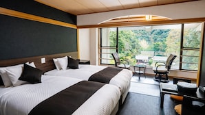 Ein Hotelzimmer mit zwei Betten, einem Schreibtisch, einem Stuhl und einem großen Fenster mit Blick ins Grüne.