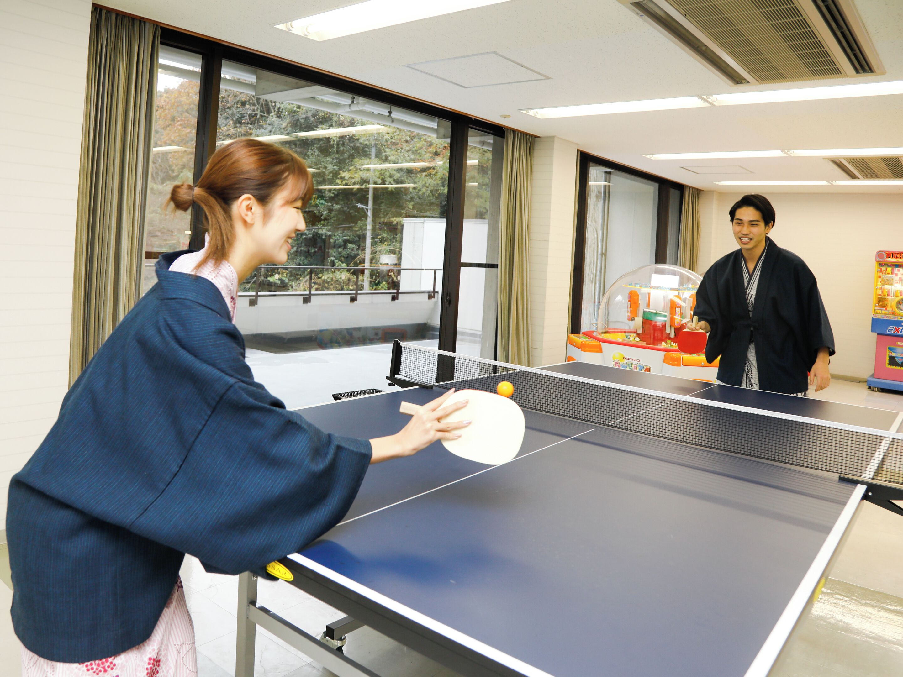 A ping pong table in a room with large windows and a vending machine.