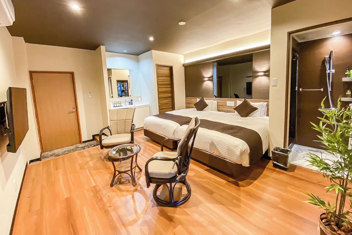 Ein modernes Hotelzimmer mit einem großen Bett, zwei Stühlen, einem kleinen Tisch, einem Spiegel und einer Duschkabine.