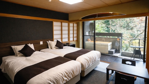 Ein Hotelzimmer mit zwei Betten, einem Schreibtisch und Blick auf einen Balkon mit Sitzgelegenheit.