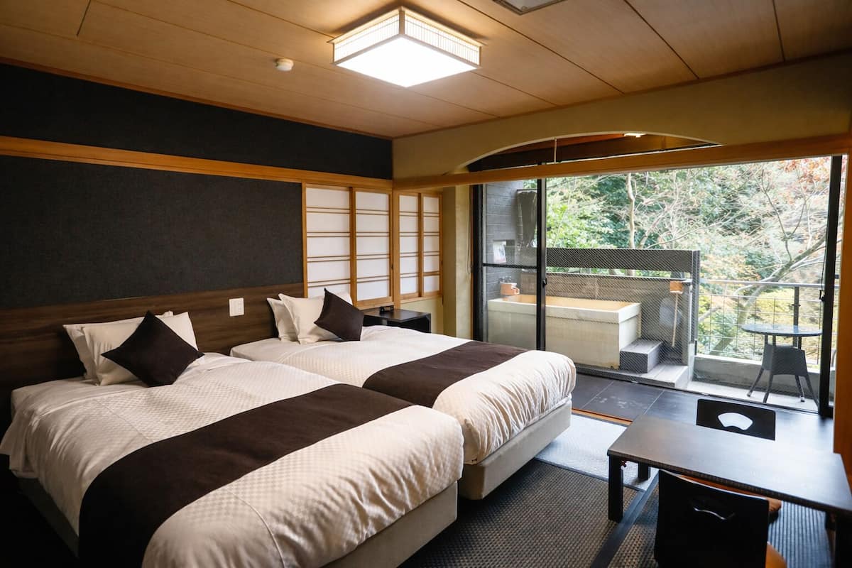 Ein Hotelzimmer mit zwei Betten, einem Schreibtisch und Blick auf einen Balkon mit Sitzgelegenheit.