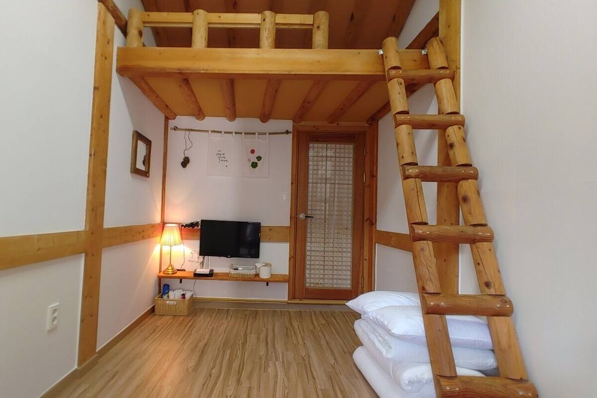 Ein kleiner Raum mit Holzbalkendecke, einem Fernseher, einer Lampe und einer Leiter.