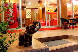 A hotel lobby with a Coca-Cola vending machine, a decorative elephant statue, a Dream Hotel sign, and a seating area with red sofas and black chairs.