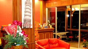 A cozy living room with a red sofa, a wooden coffee table, and a large window with a view of the outside. - Tropical Sunset Hotel Patong (Patong)
