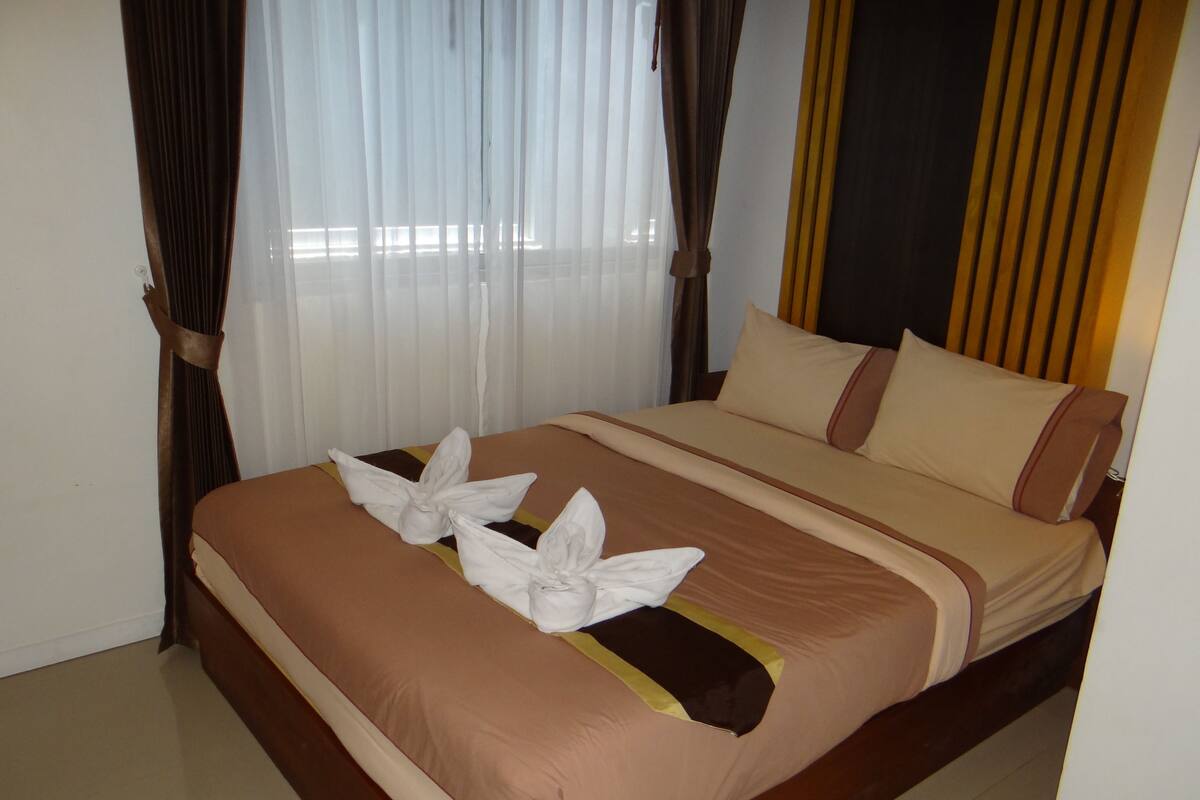 A neatly made bed with a brown and beige color scheme, white towels arranged in a bow shape, and a wooden headboard.