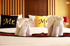 A neatly made bed with two towels folded on the bed, a black pillow with "Mr." in gold lettering, and a yellow pillow with "Mr." in black lettering.