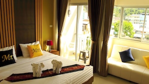A hotel room with a large bed, a sofa, and a view of the city. - Tropical Sunset Hotel Patong (Patong)