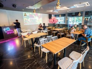 A modern cafe with wooden tables and chairs, a projection screen, and a neon sign. - Koho Hotel (Johor Bahru)