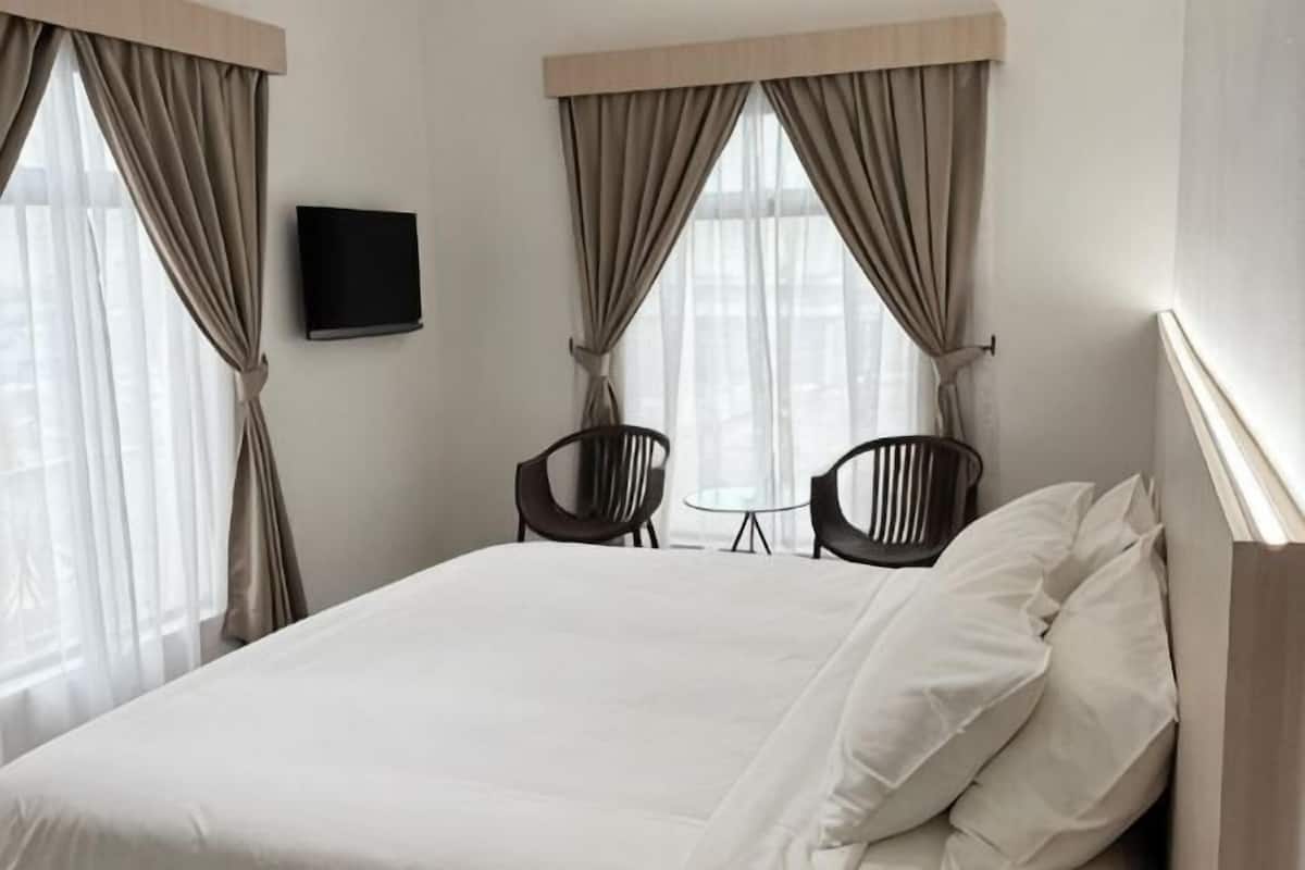 A hotel room with a bed, two chairs, a small table, and a TV on the wall.
