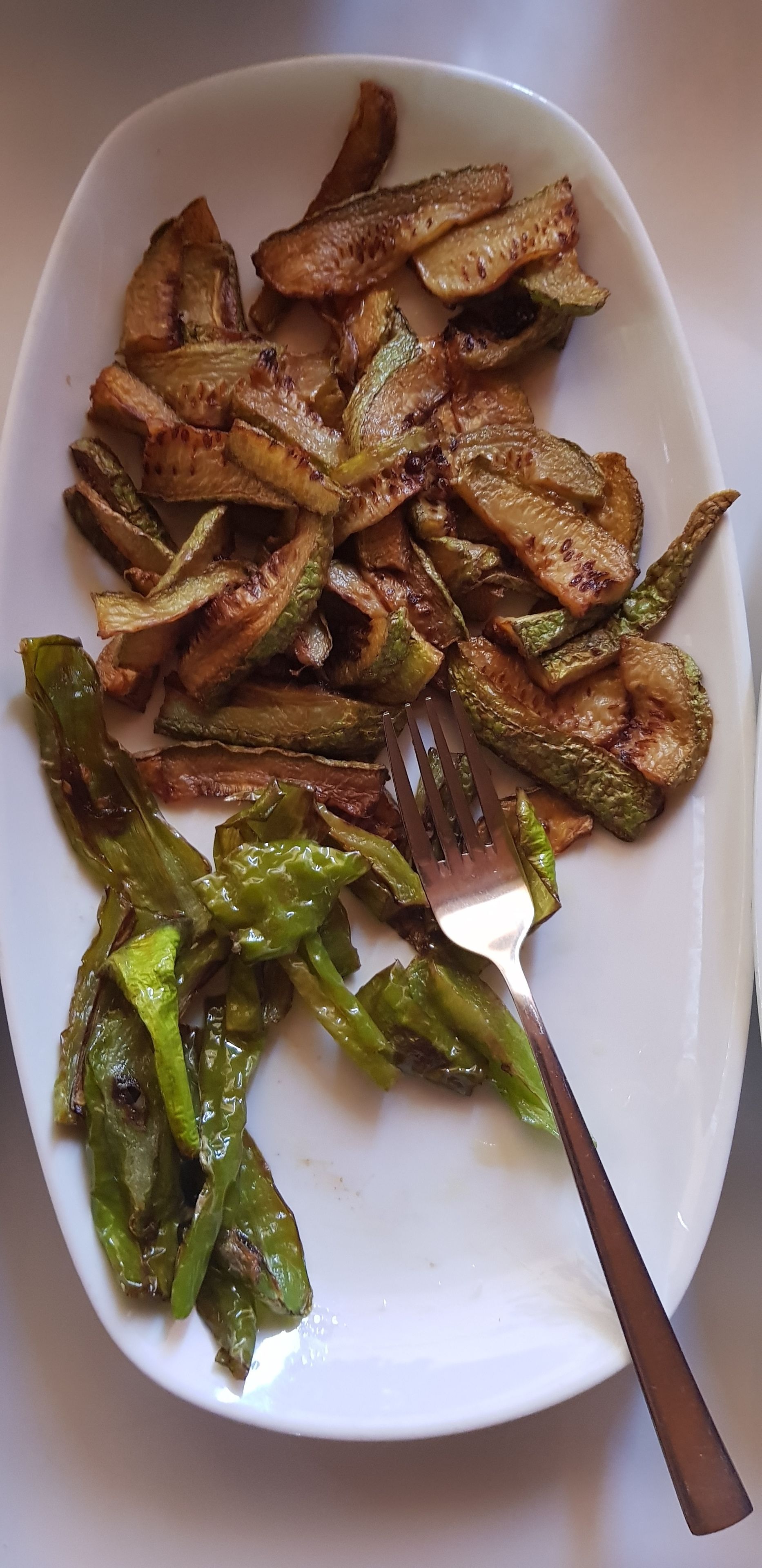 Prato branco com legumes assados e um garfo.