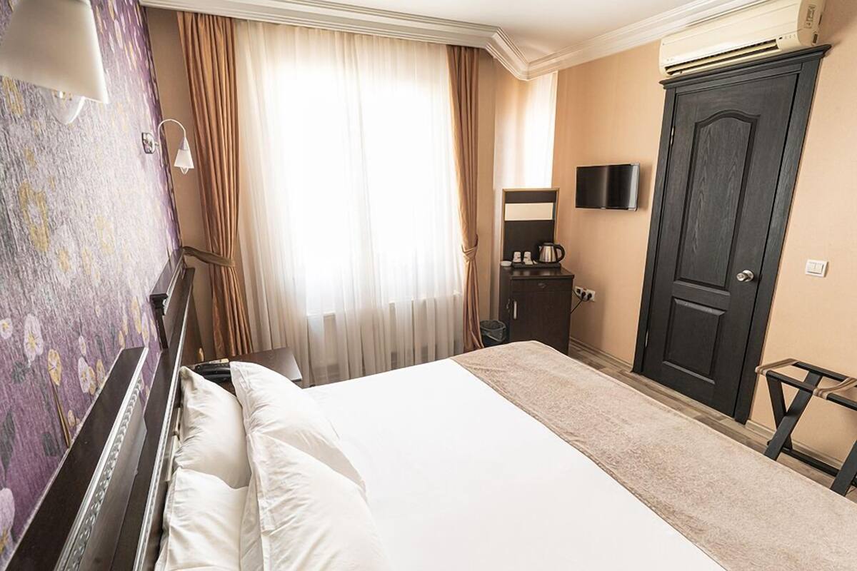 Een hotelkamer met een bed, een kledingkast, een bureau met stoel, een televisie en een raam met gordijnen.