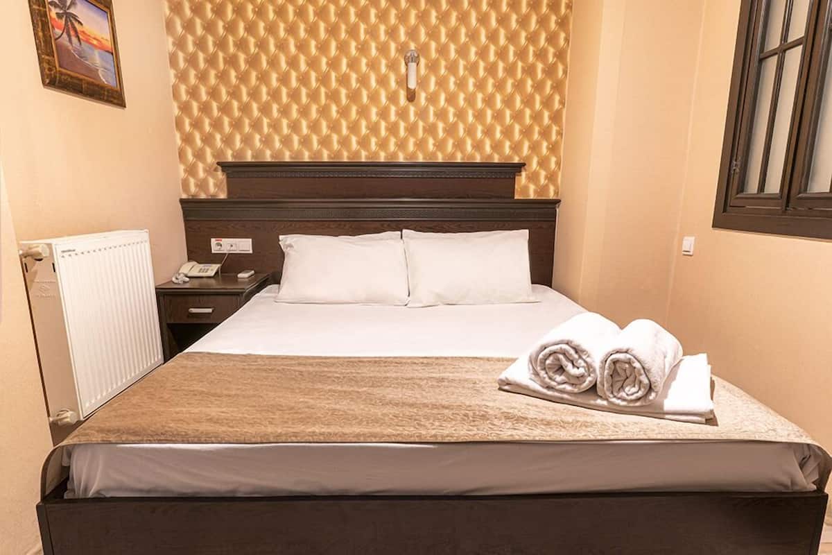 Een keurig opgemaakt bed met witte lakens en een bruine deken, een nachtkastje met een telefoon en een lamp, en een wand met behangpapier met een patroon.