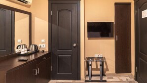 Habitación de hotel con puerta de madera oscura, una mesa pequeña con un televisor y un espejo sobre el mostrador.