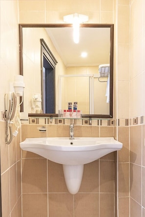 A bathroom with a white sink, a mirror, and a hairdryer on the wall.
