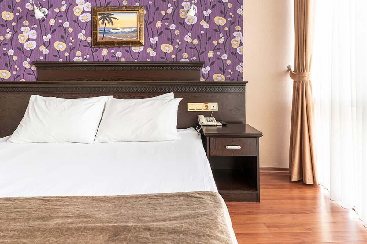 Een hotelkamer met een bed, een nachtkastje met een telefoon, en een wand met bloemenpatroon en een lijst.