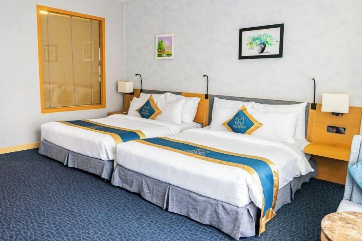 Habitación de hotel con dos camas, un ventanal con persianas, una mesita y una silla.