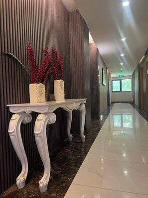 A hallway with a polished marble floor, a white ornate table with two vases, and a vertical wooden panel wall.