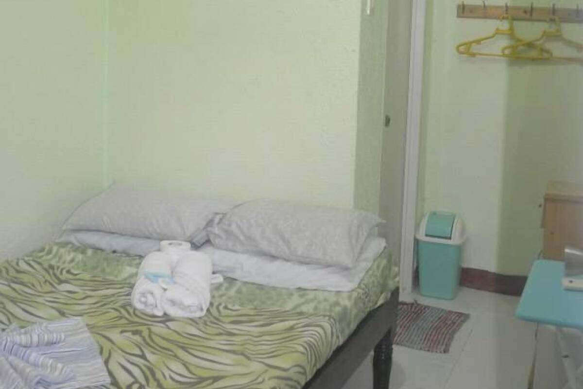 A small, clean room with a bed, a wall-mounted picture, a small table, and a chair.