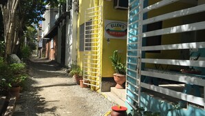 Un estrecho callejón con un edificio amarillo, un cartel que dice 'Ellen's Resort & Apartments' y plantas en macetas a lo largo del camino.