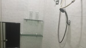 Un baño pequeño con azulejos, un inodoro, una estantería de cristal, un cabezal de ducha y un dispensador de papel higiénico.