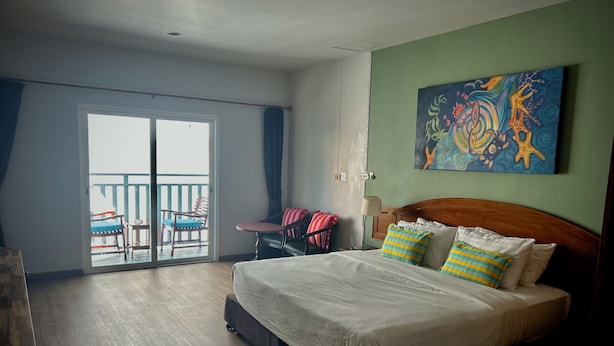 A hotel room with a bed, a balcony with chairs, and a painting on the wall. - Sugar and Spice Inn (Karon)